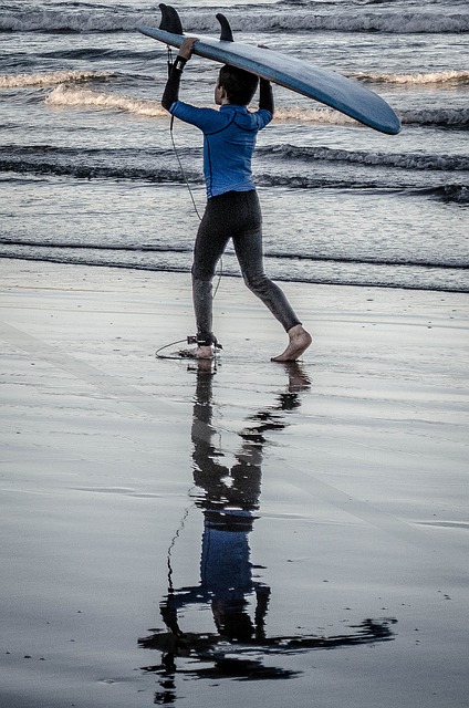 A young boy carries a surf board on his head across the sand towards the water